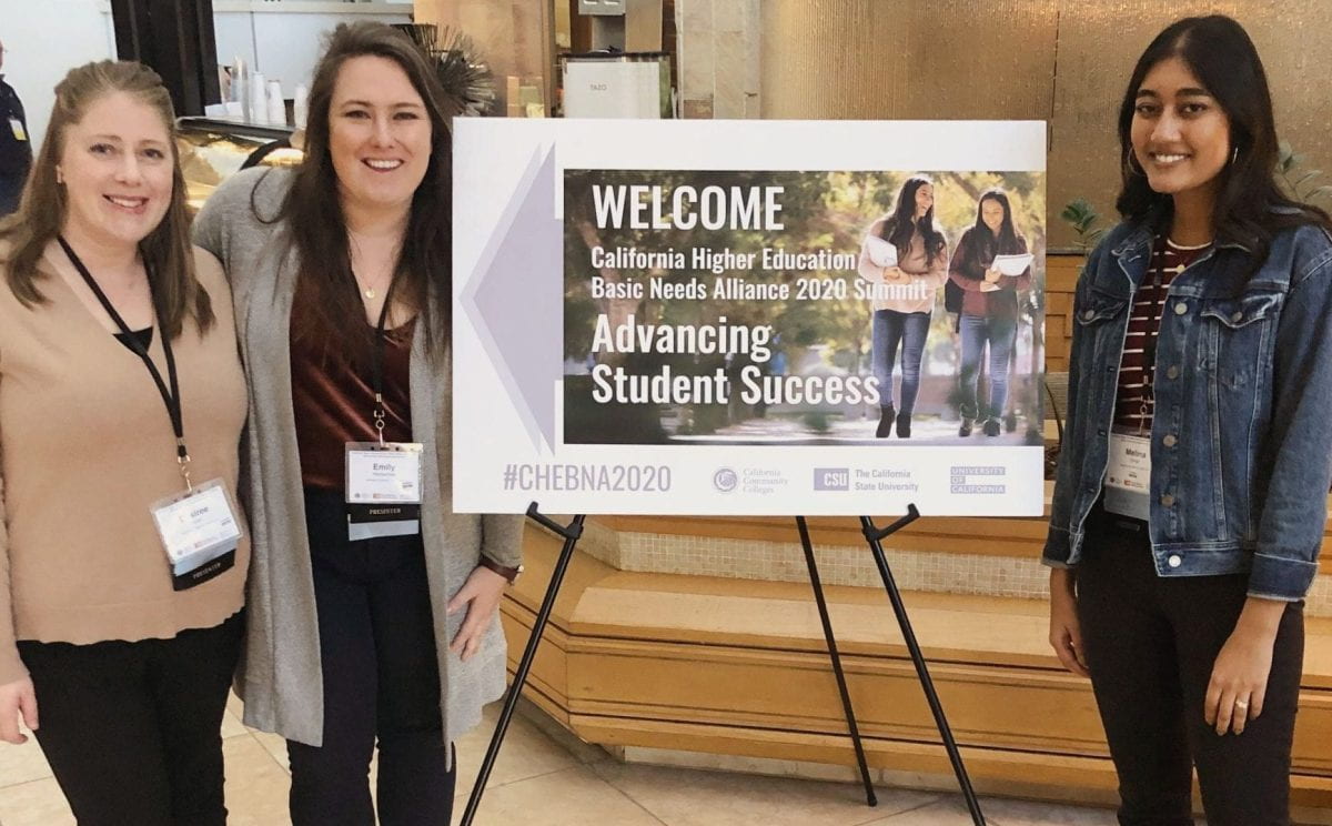three students standing around conference signage